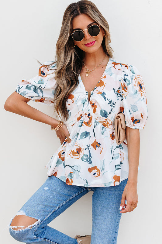 Woman wearing a floral blouse and jeans with sunglasses on a plain background